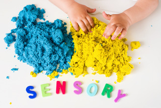 Child's hands playing in blue and yellow kinetic sand